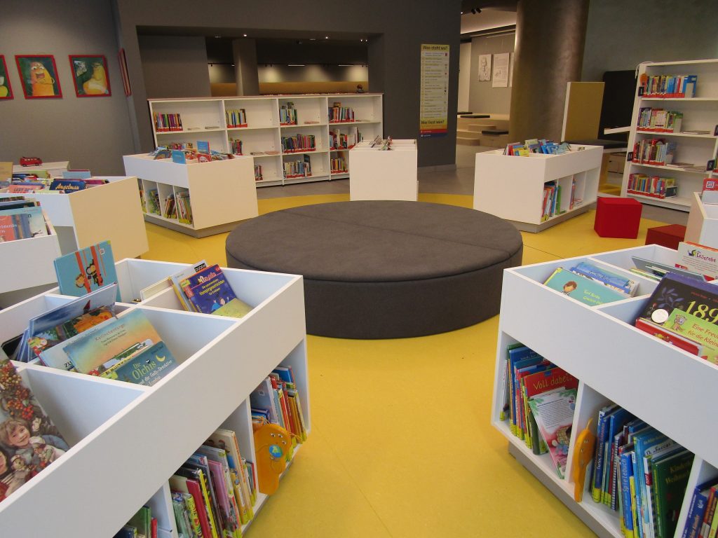 Niedrige Bücherregale mit Kinderbüchern und Sitzecke. 