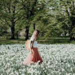 Junge Frau mit Rucksack spaziert über Blumenwiese.
